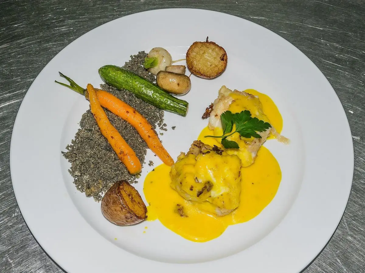 Plato blanco con rape en salsa amarilla, patatitas, zanahorias y judías verdes