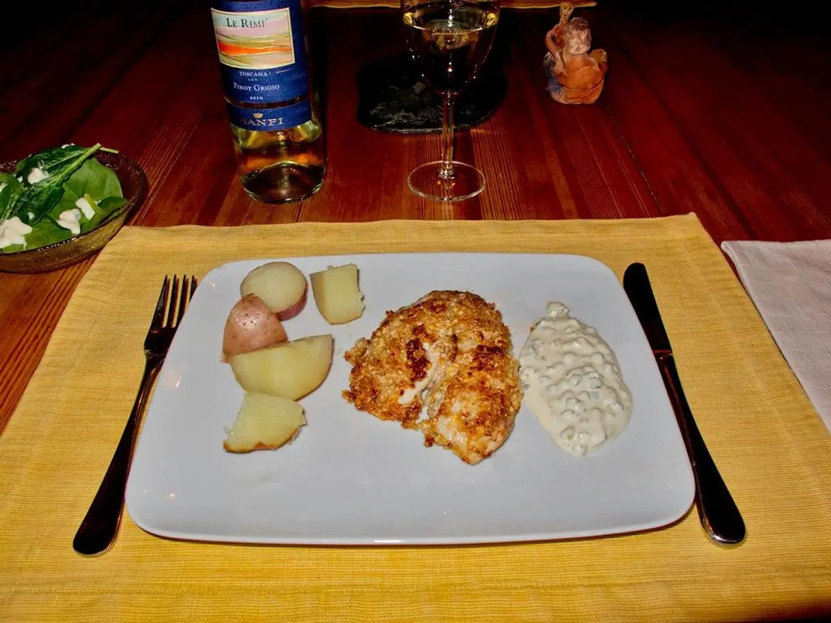 Plato gris con filete de pescado dorado, patatas cocidas pequeñas y salsa blanca sobre un mantel amarillo