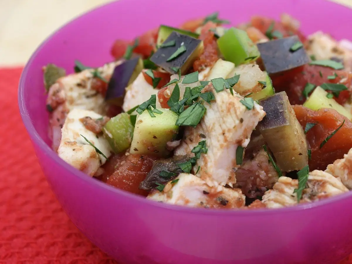 Cuenco con pollo desmenuzado y ratatouille de berenjena, calabacín y tomate con hierbas