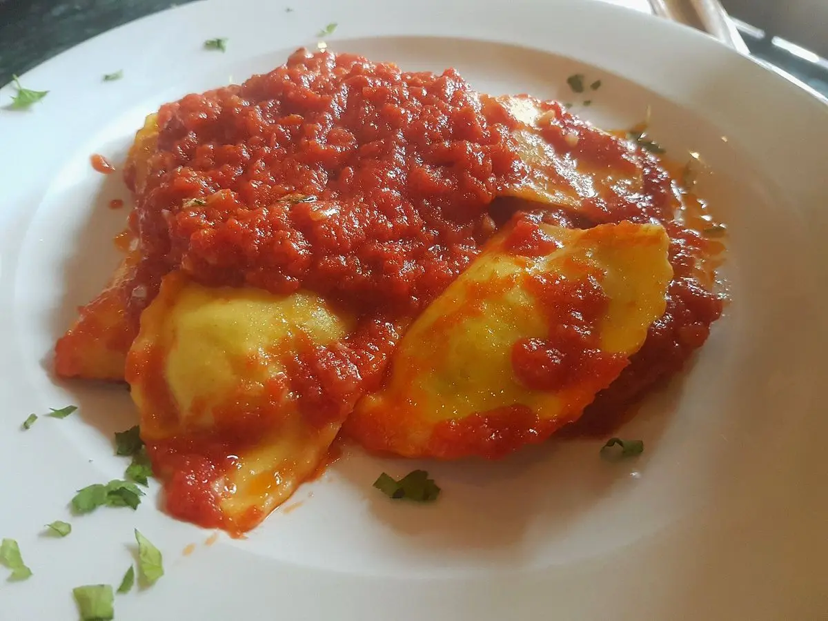 Raviolis rellenos cubiertos de salsa de tomate en un plato blanco