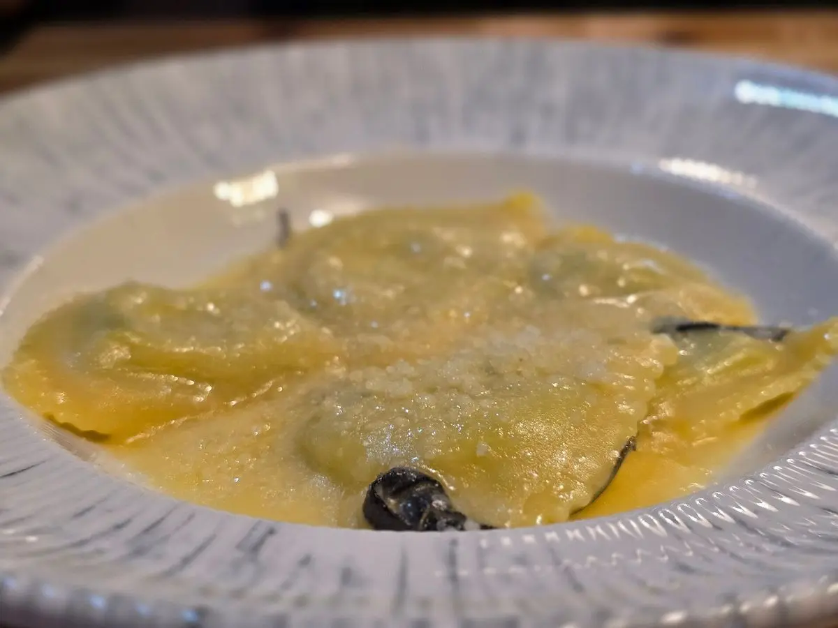 Raviolis rellenos con mantequilla, salvia y queso rallado en un plato hondo blanco
