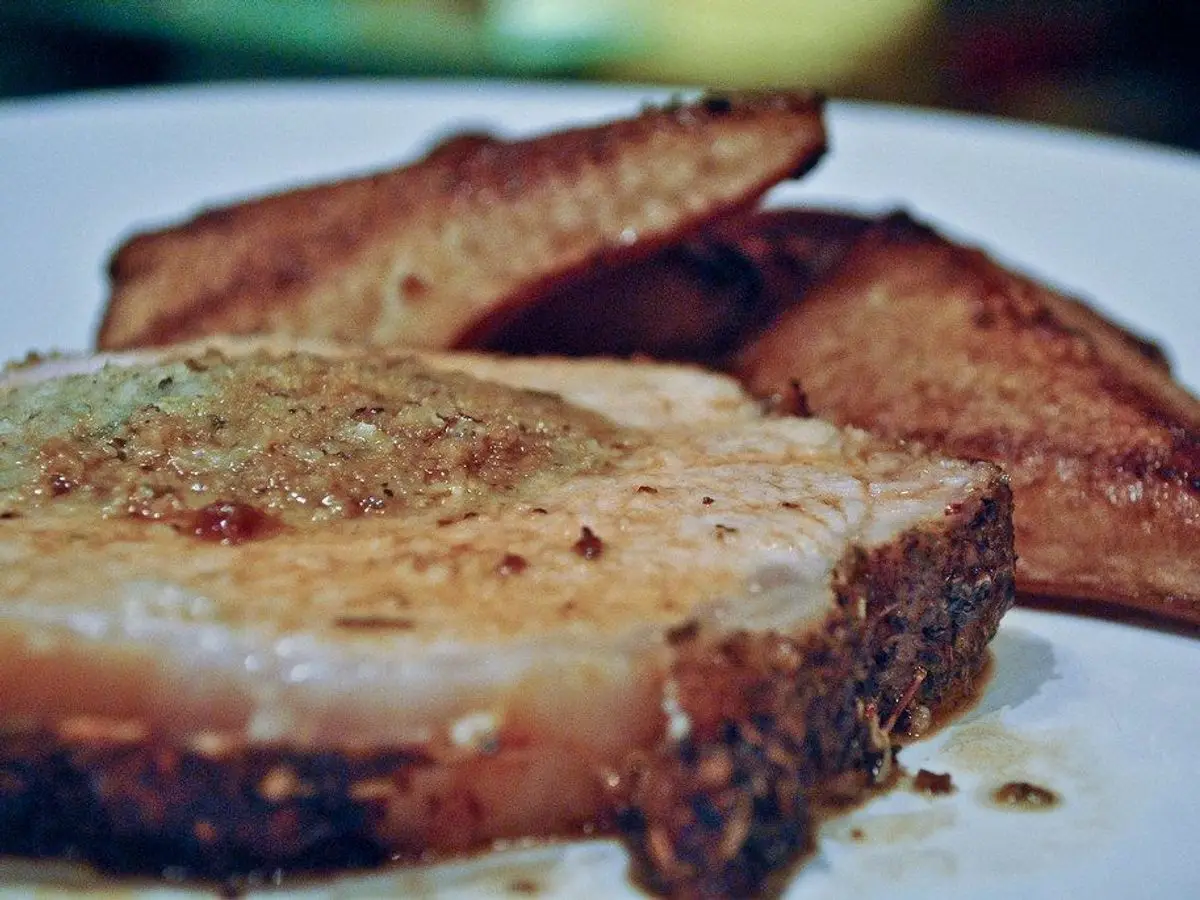 Filete grueso de lomo de cerdo asado con pimienta junto a rebanadas de pan en un plato