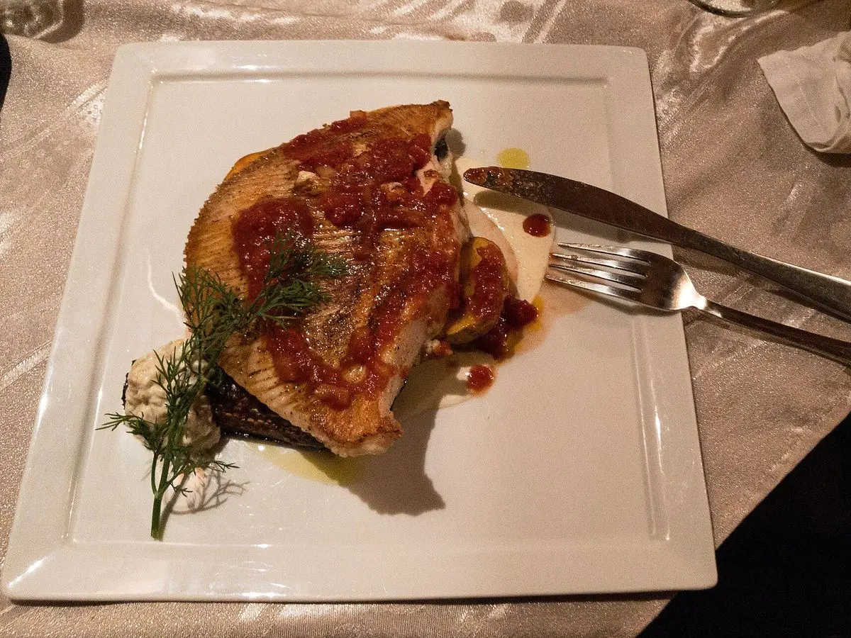 Ala de raya asada con salsa y eneldo fresco en un plato blanco cuadrado con cubiertos