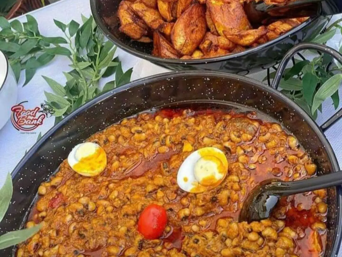 Sartén de judías en salsa roja de tomate con huevo duro, y plátano macho frito en un cuenco al fondo