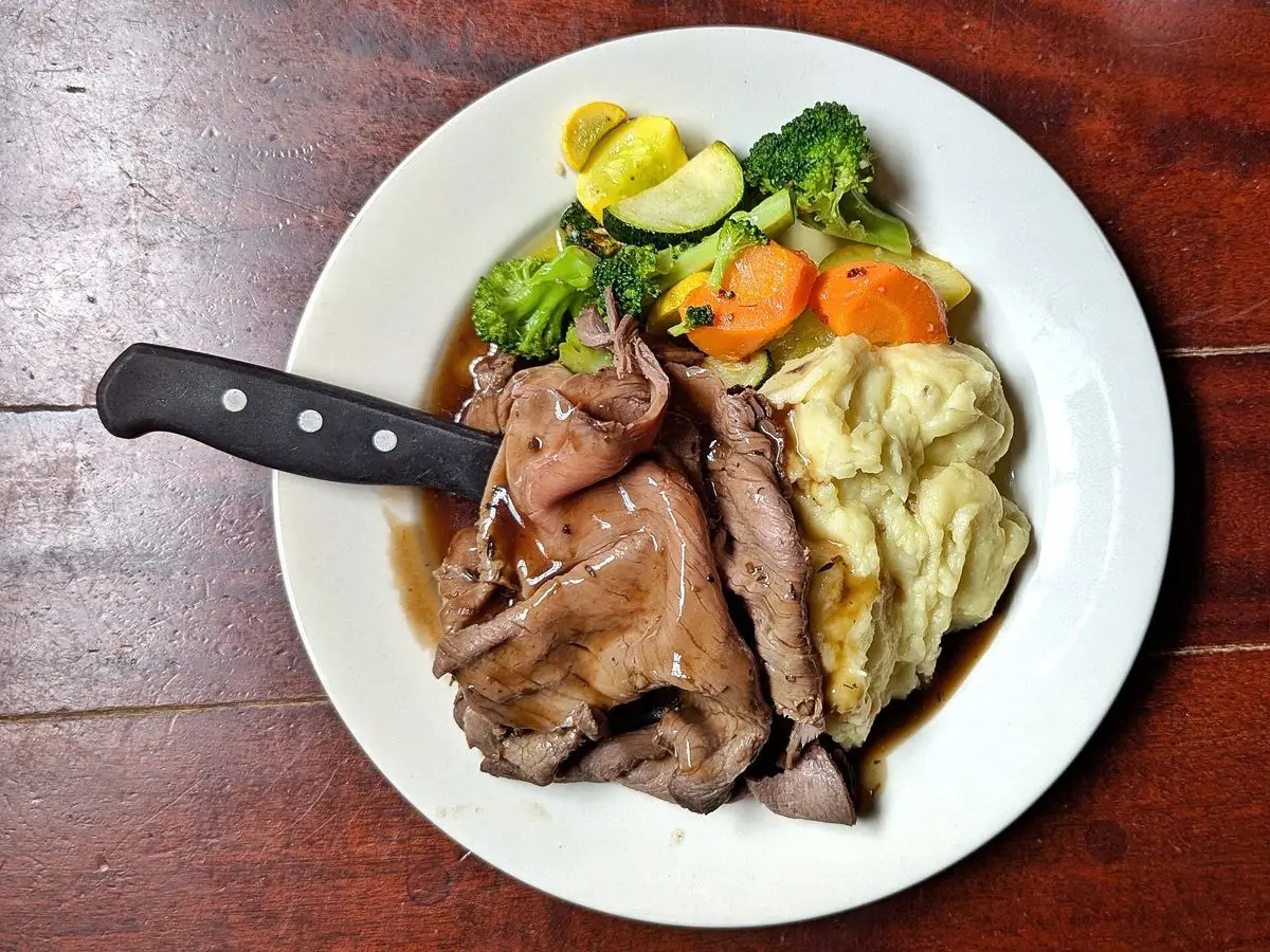 Plato blanco con lonchas de ternera asada, brócoli, zanahoria y puré, visto desde arriba