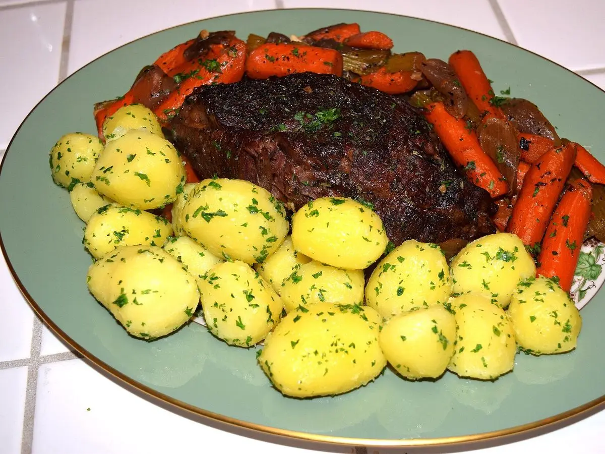 Asado de ternera en un plato verde con zanahorias y patatas pequeñas con perejil