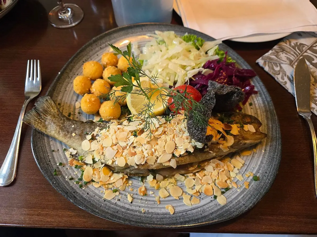 Trucha con almendra laminada servida con ensalada, patatas y limón en un plato grande