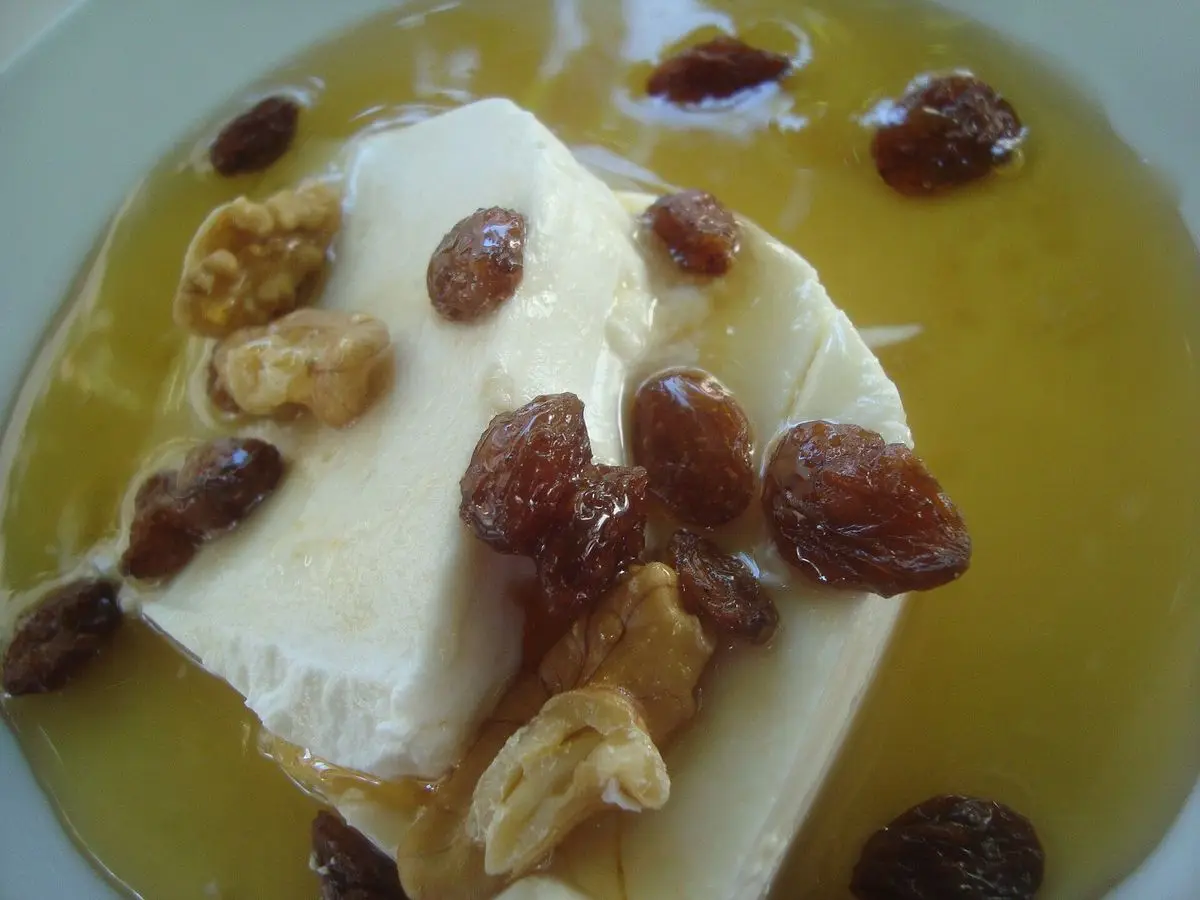 Trozo de queso fresco blanco bañado en miel con pasas y frutos secos en un plato