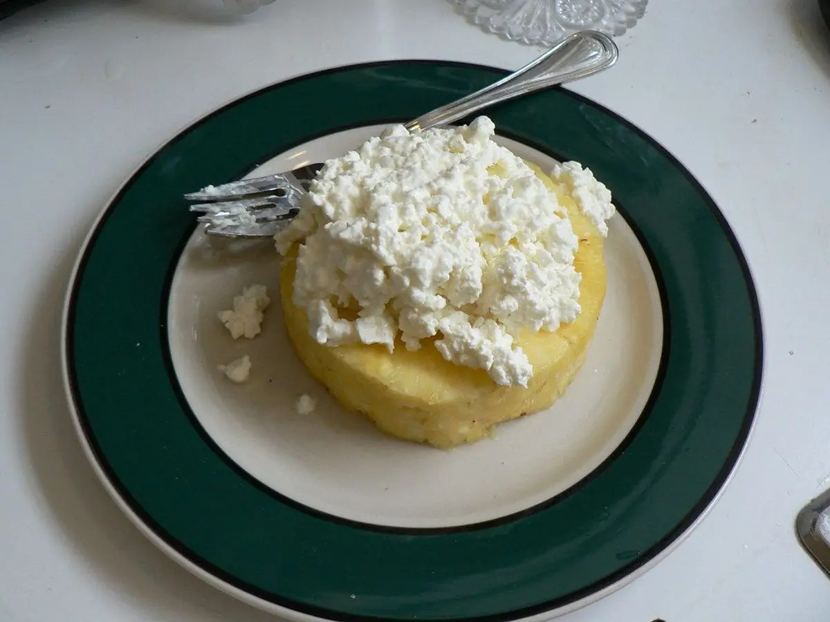 Rodaja de piña con requesón por encima en un plato con borde verde y un tenedor