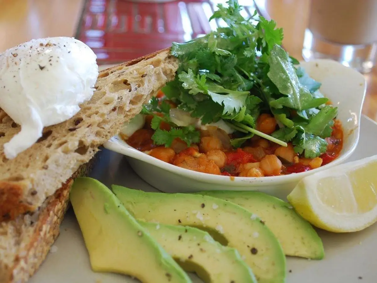 Plato de garbanzos horneados en salsa de tomate con huevo escalfado, tostada y aguacate