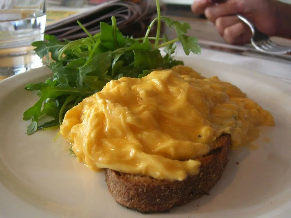Huevos revueltos cremosos sobre una rebanada de pan tostado con hojas de rúcula