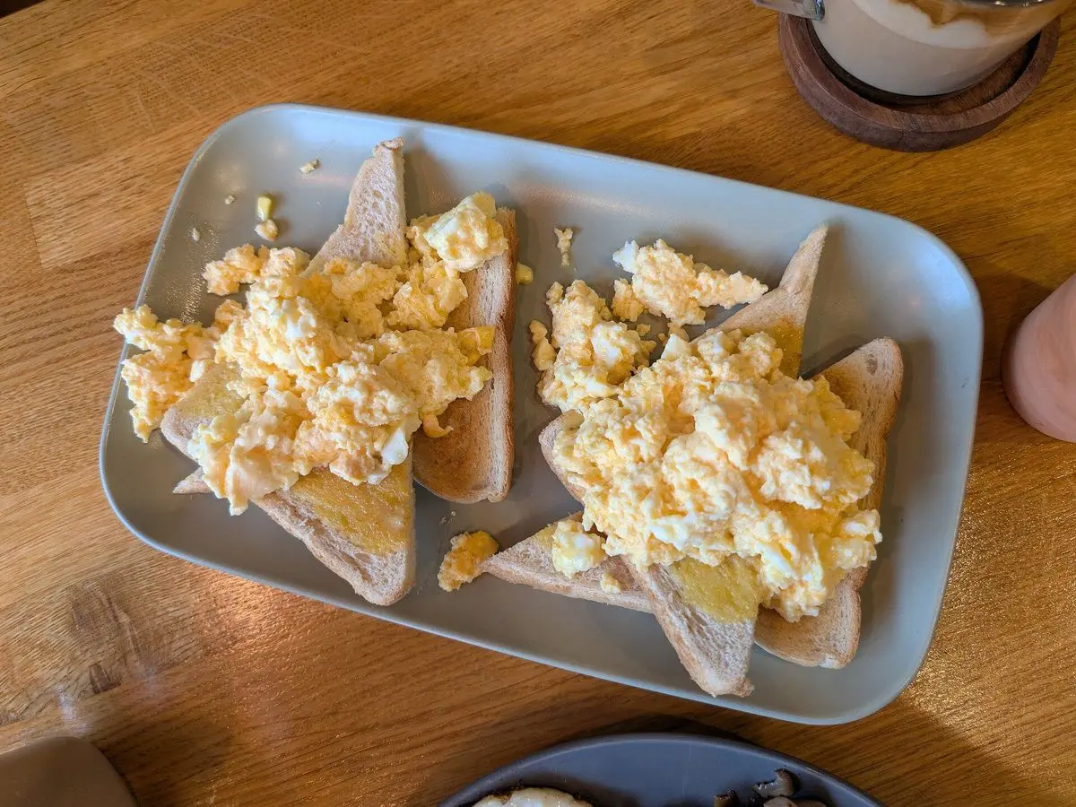 Fuente alargada con dos tostadas cubiertas de huevo revuelto cremoso sobre una mesa de madera