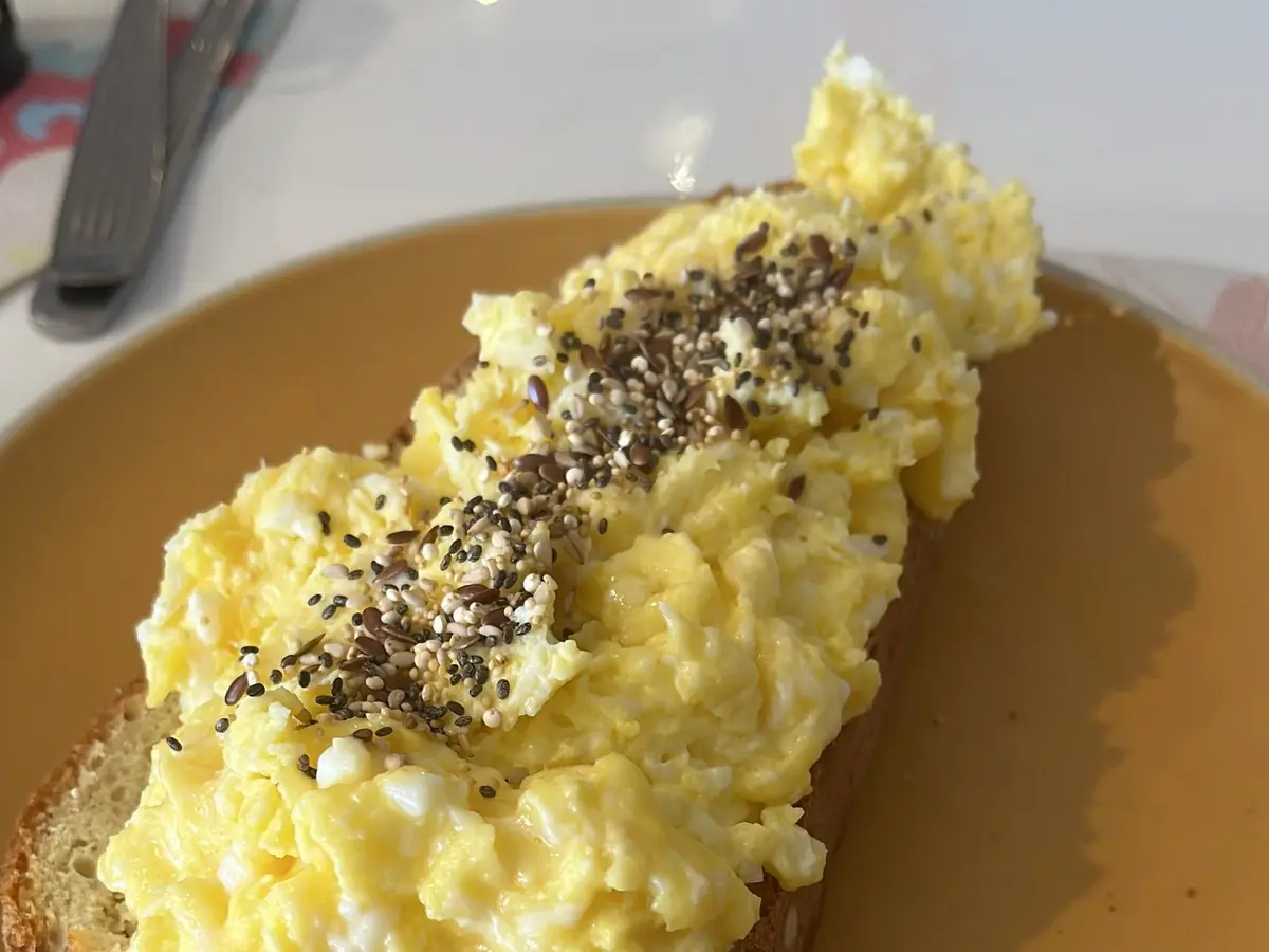 Huevos revueltos cremosos con semillas sobre una rebanada de pan tostado en un plato amarillo