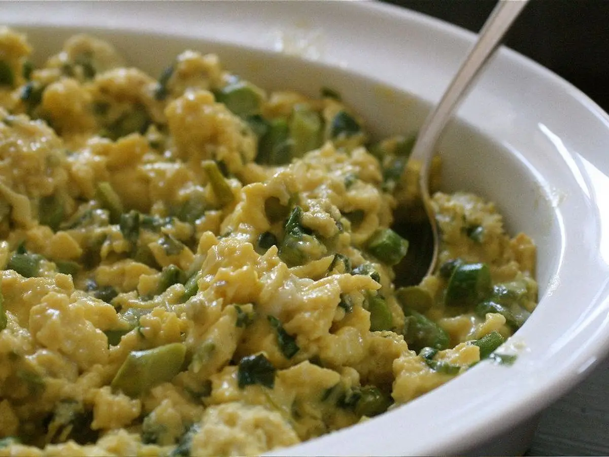 Huevos revueltos con trocitos de espárrago verde en una fuente blanca con una cuchara