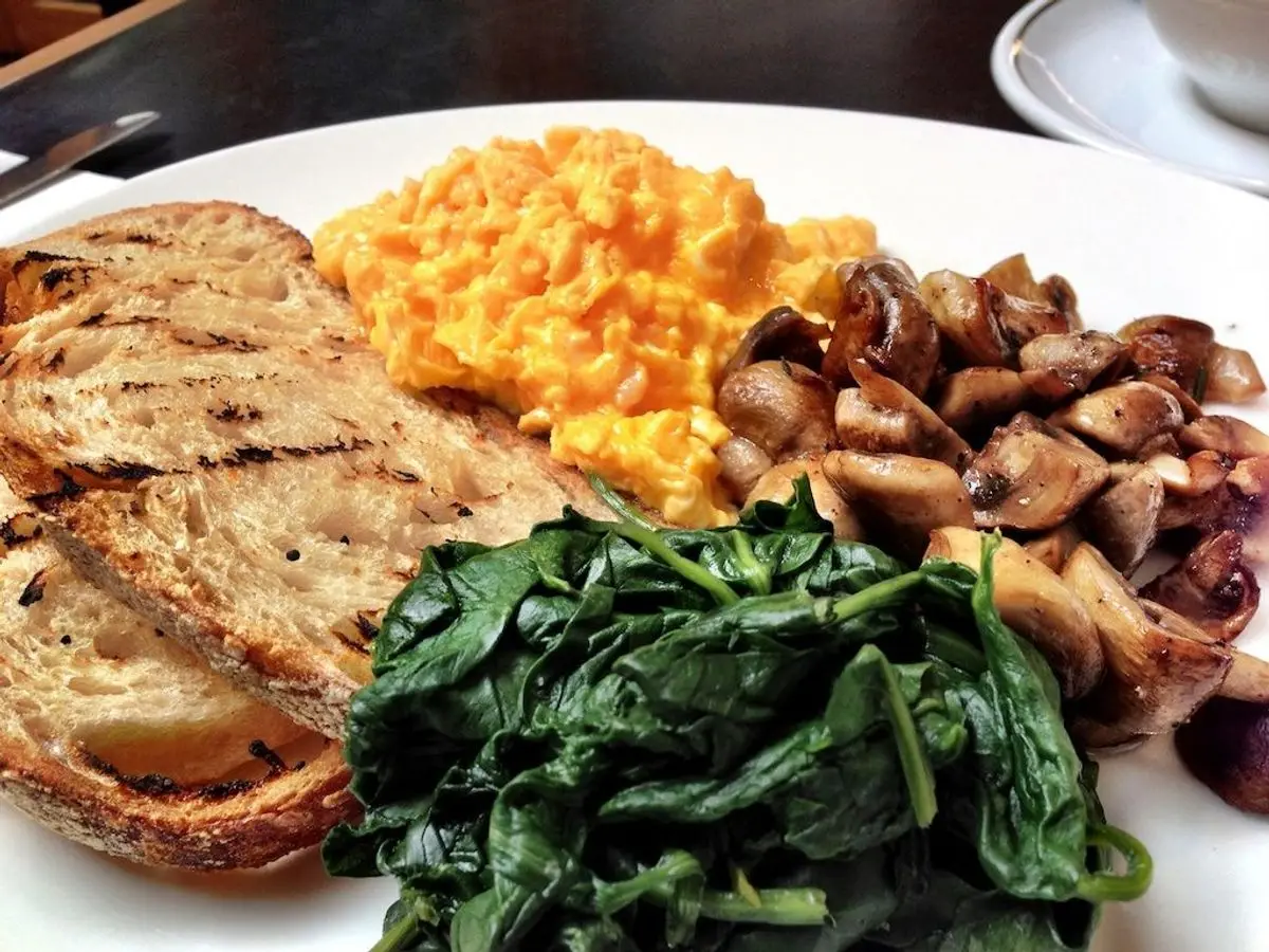 Plato con huevos revueltos, champiñones salteados, espinacas y tostadas de pan