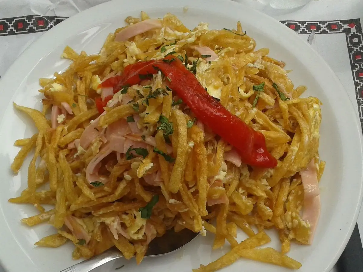 Plato blanco de revuelto de patata en tiras fritas con huevo, jamón y tiras de pimiento rojo