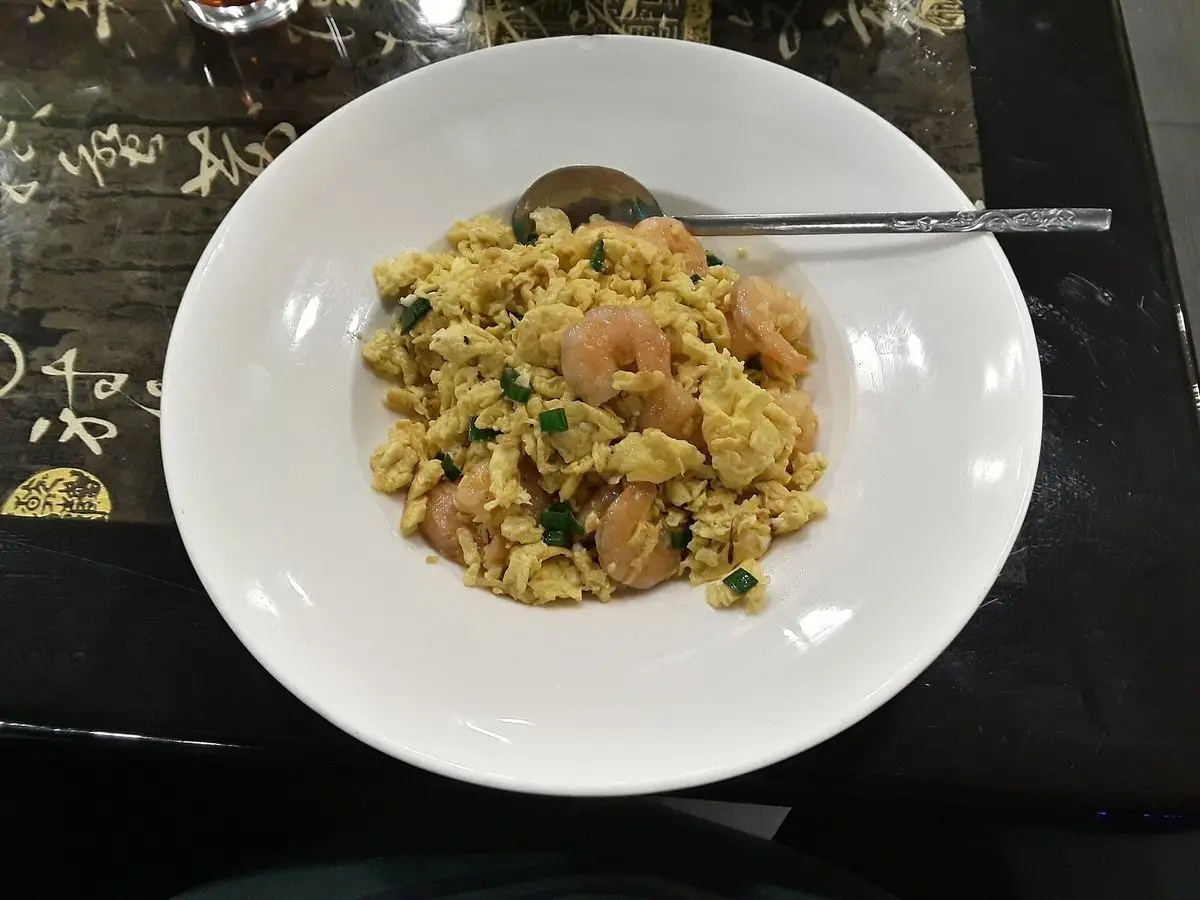 Plato blanco de huevos revueltos con gambitas pequeñas, visto desde arriba sobre una mesa oscura