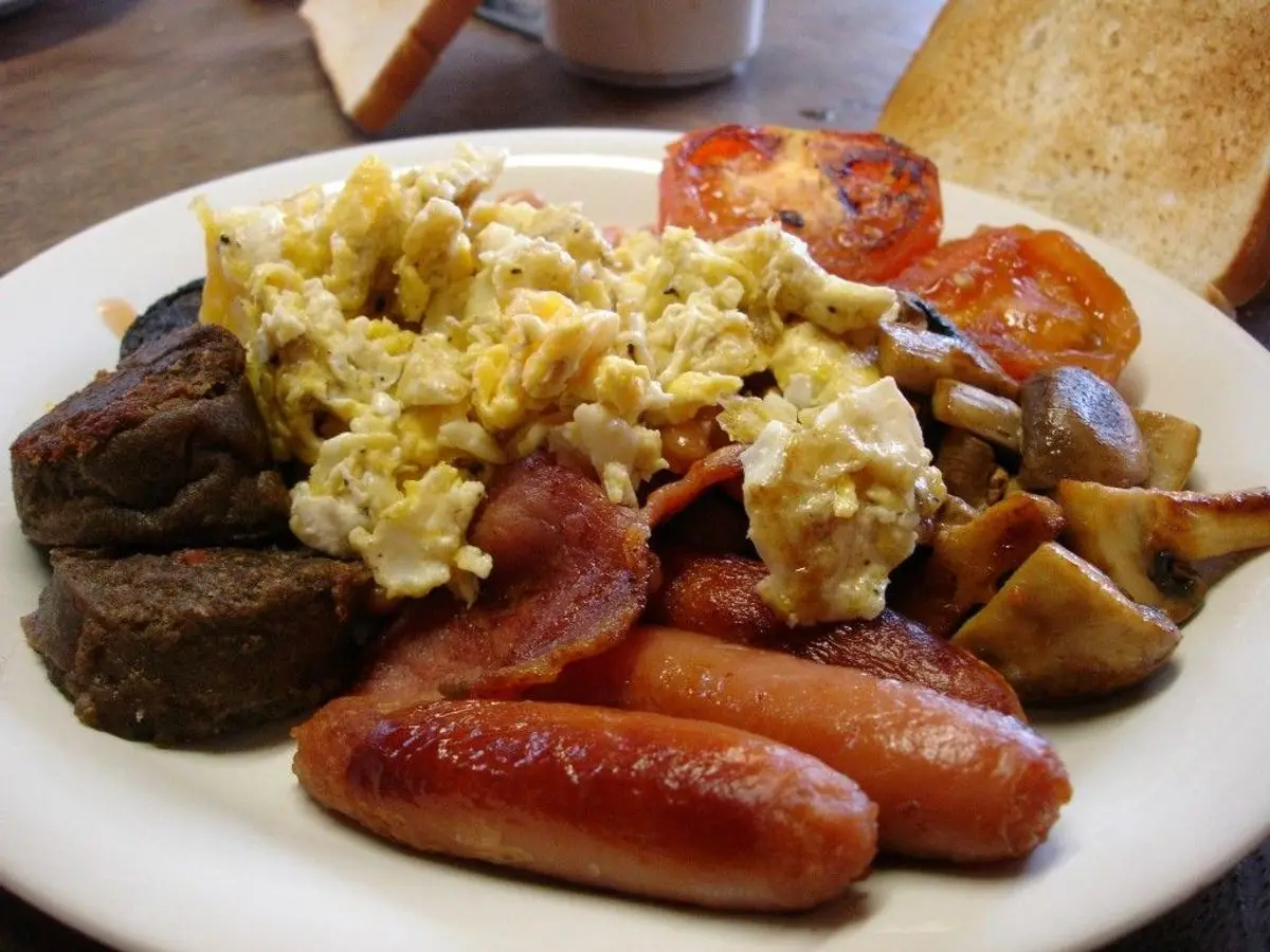 Plato con huevos revueltos, morcilla, salchichas y tomate