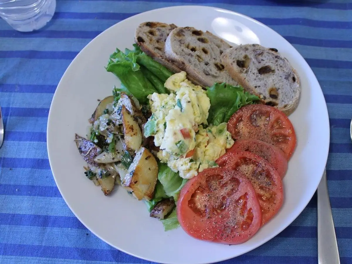 Plato con huevo revuelto, patatas salteadas, ensalada, rodajas de tomate y pan