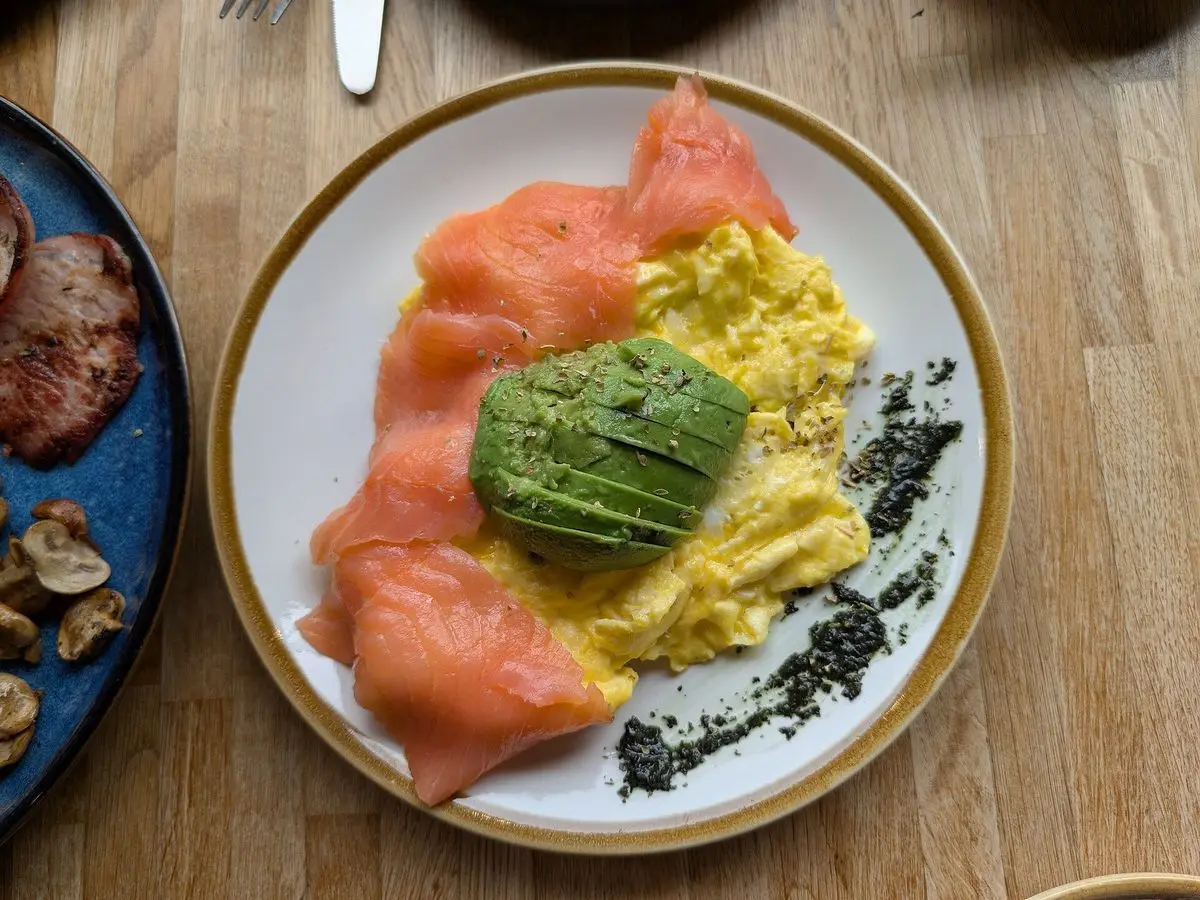 Plato con huevos revueltos, lonchas de salmón ahumado y aguacate sobre una mesa de madera