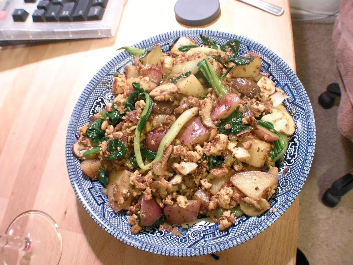 Plato de loza azul con tofu revuelto, espinacas y verduras salteadas sobre una mesa de madera