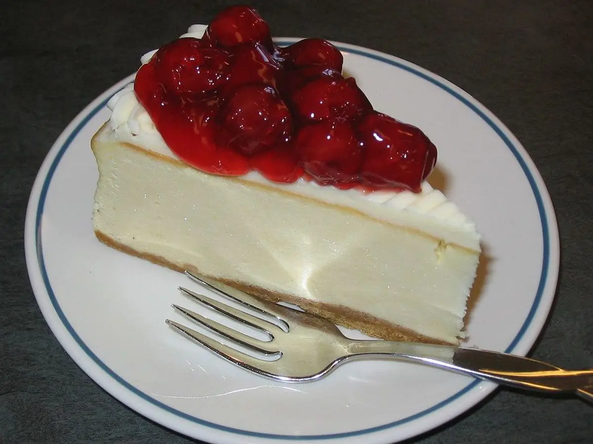Porción de tarta de queso cubierta de cerezas rojas brillantes en un plato blanco