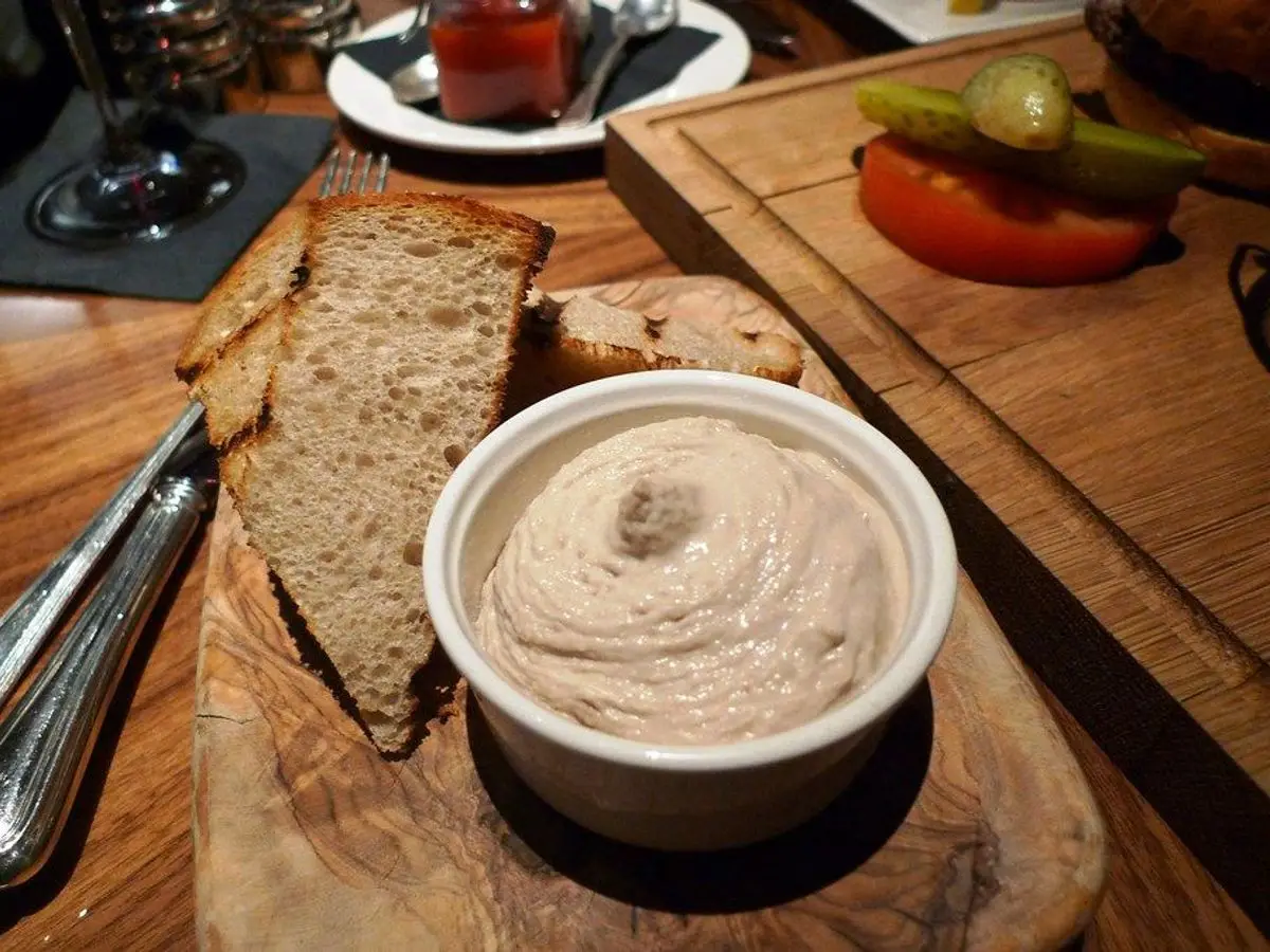 Ramequín de paté cremoso de pescado con rebanadas de pan sobre una tabla de madera