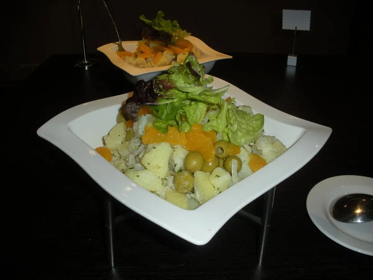 Fuente blanca con ensalada de patata cocida, bacalao desmigado, aceitunas verdes, gajos de naranja y lechuga