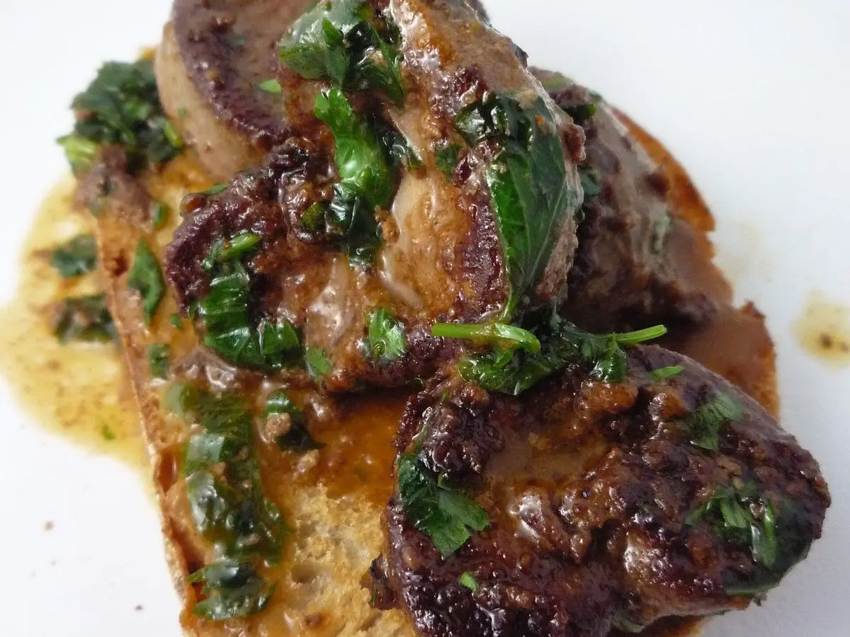 Riñones salteados en salsa especiada sobre una tostada de pan, con perejil picado, en un plato blanco