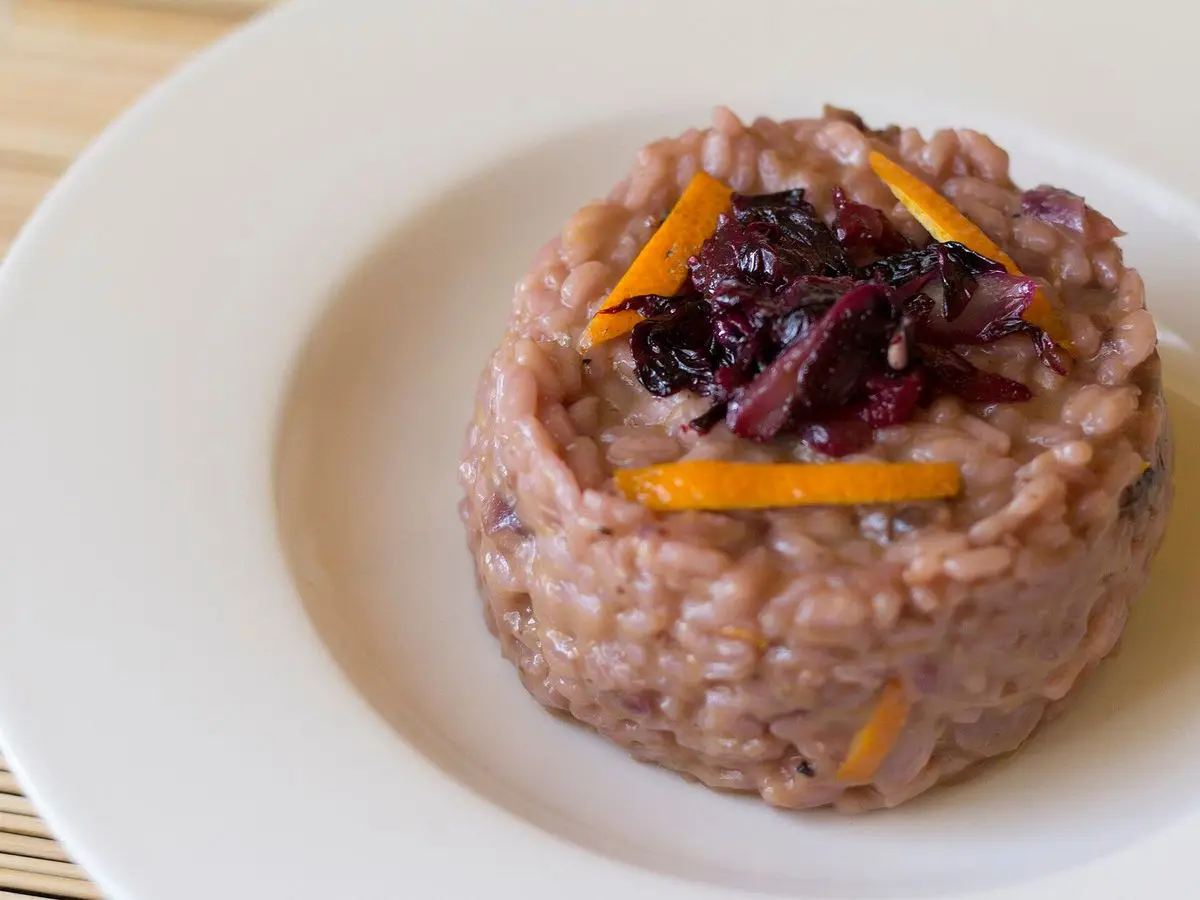 Montaje de risotto de radicchio con tiras de naranja en un plato blanco