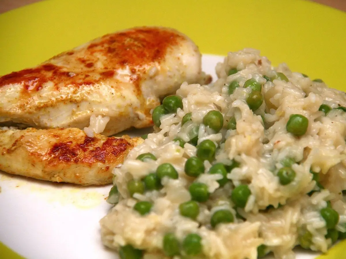 Pechuga de pollo dorada junto a risotto cremoso con guisantes sobre un plato blanco