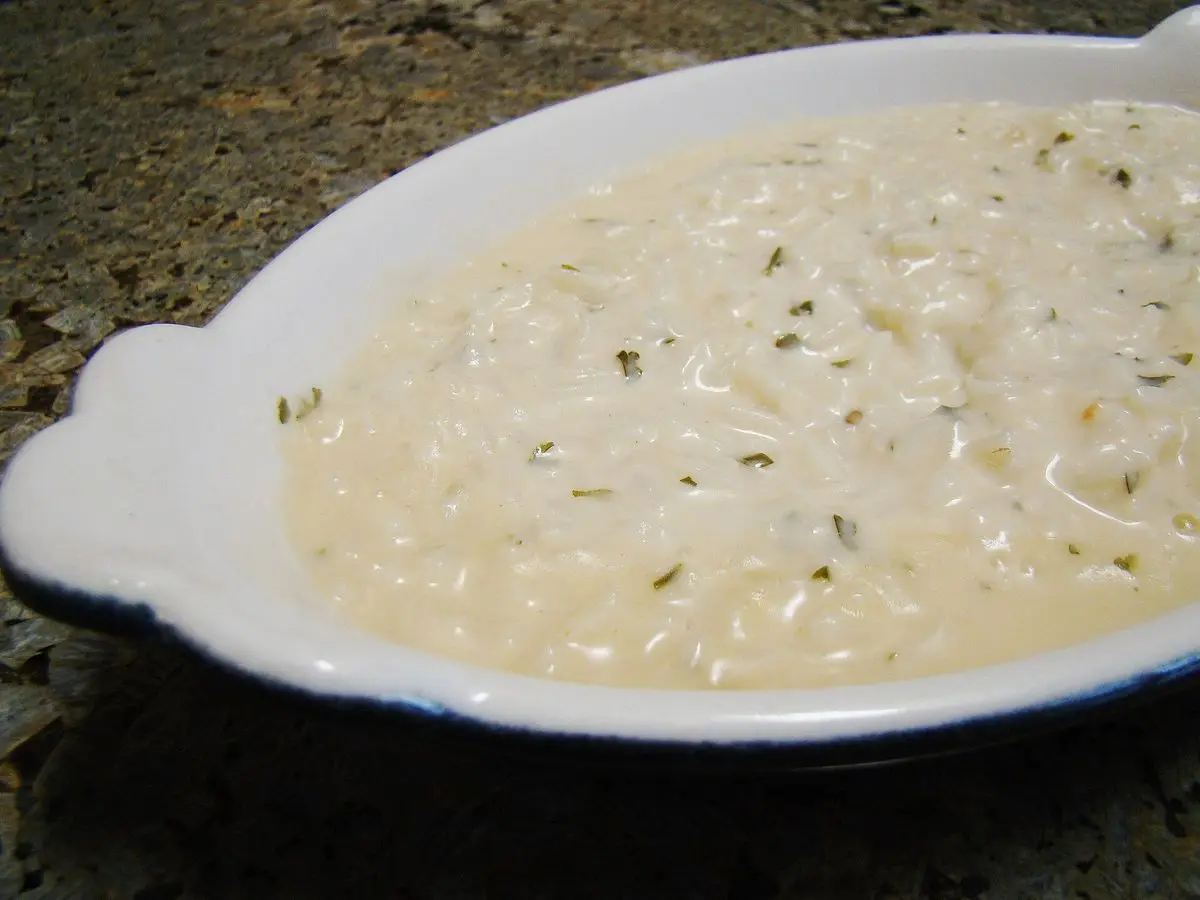 Fuente blanca de risotto cremoso con hierbas picadas sobre una encimera de granito