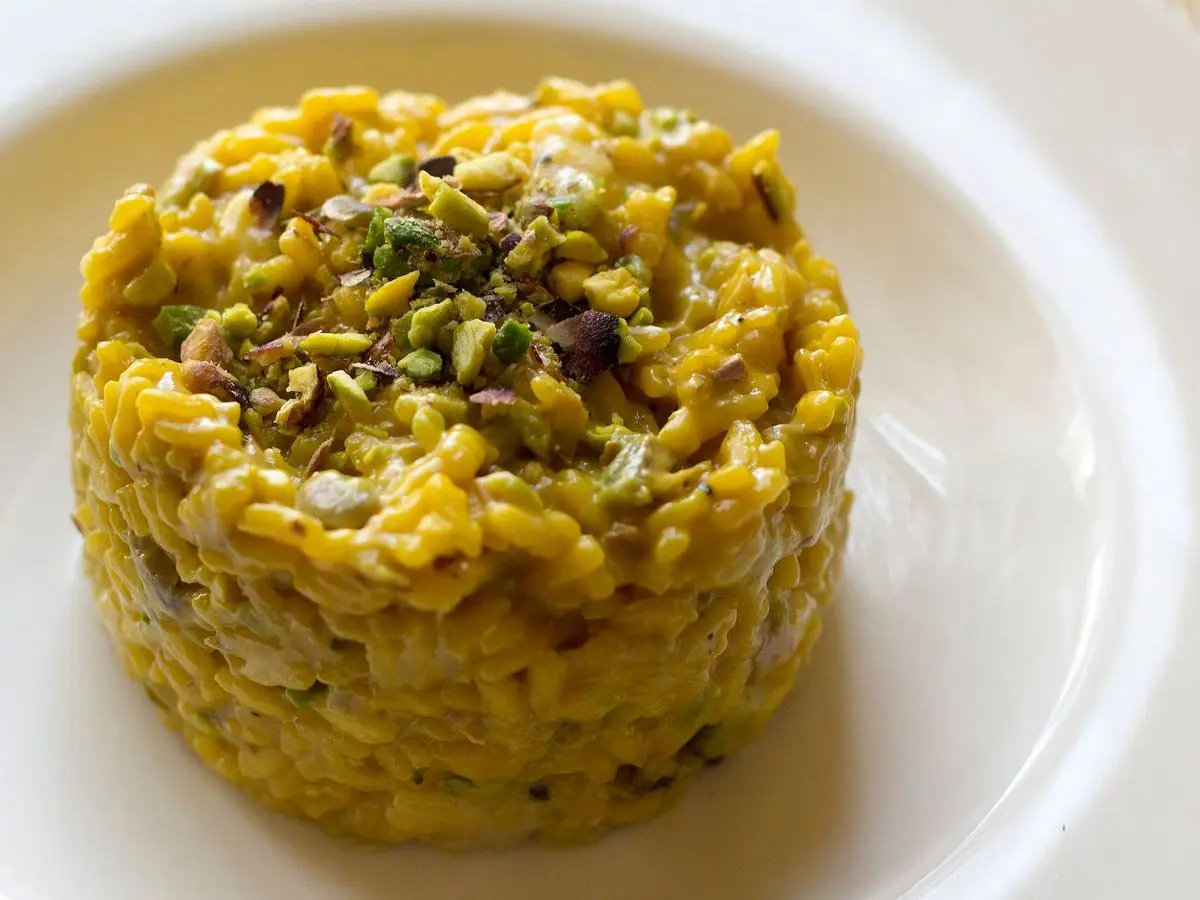 Risotto amarillo al azafrán moldeado en torre con pistachos picados sobre un plato blanco