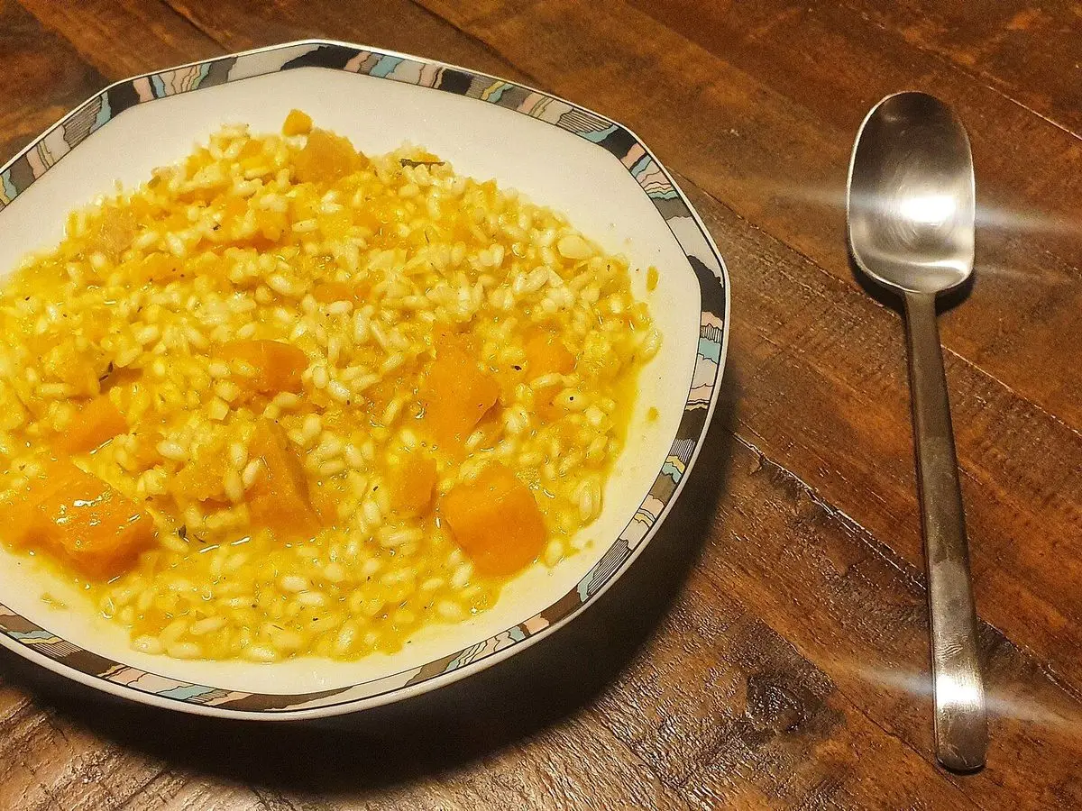 Risotto amarillo con dados de calabaza en un plato decorado sobre mesa de madera, con una cuchara