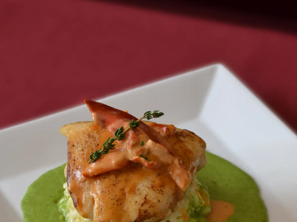 Filete de pescado a la plancha sobre risotto y salsa verde de espinacas en un plato cuadrado blanco