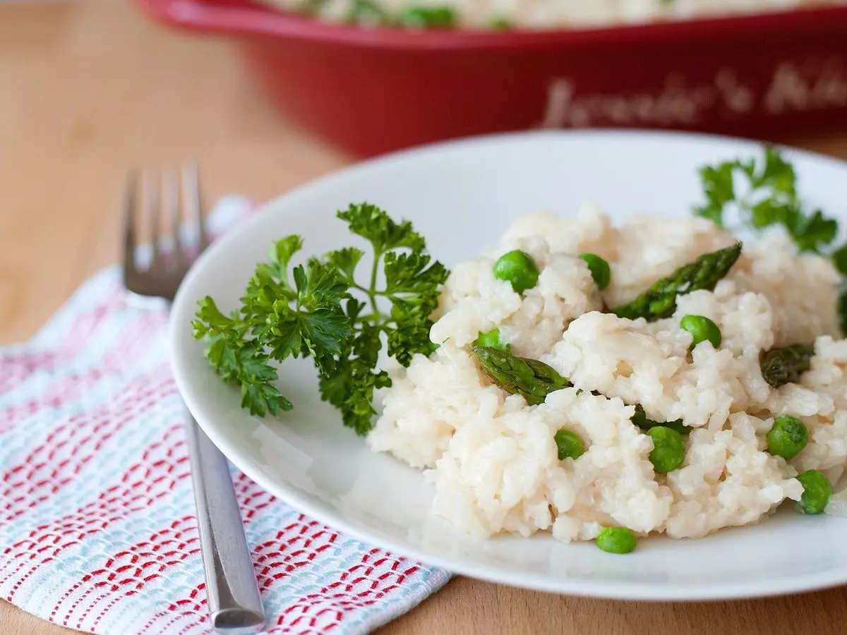 Plato blanco de risotto cremoso con guisantes y perejil sobre un paño de cuadros
