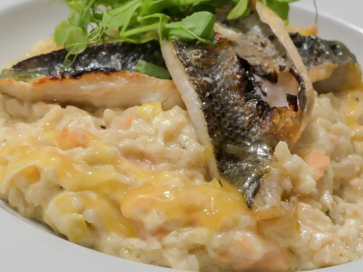 Filete de pescado con piel dorada sobre risotto cremoso y hojas verdes tiernas en un plato blanco