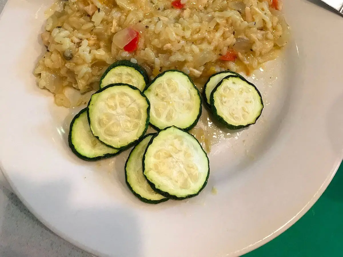Risotto cremoso con trocitos de pimiento rojo y rodajas de calabacín en un plato blanco