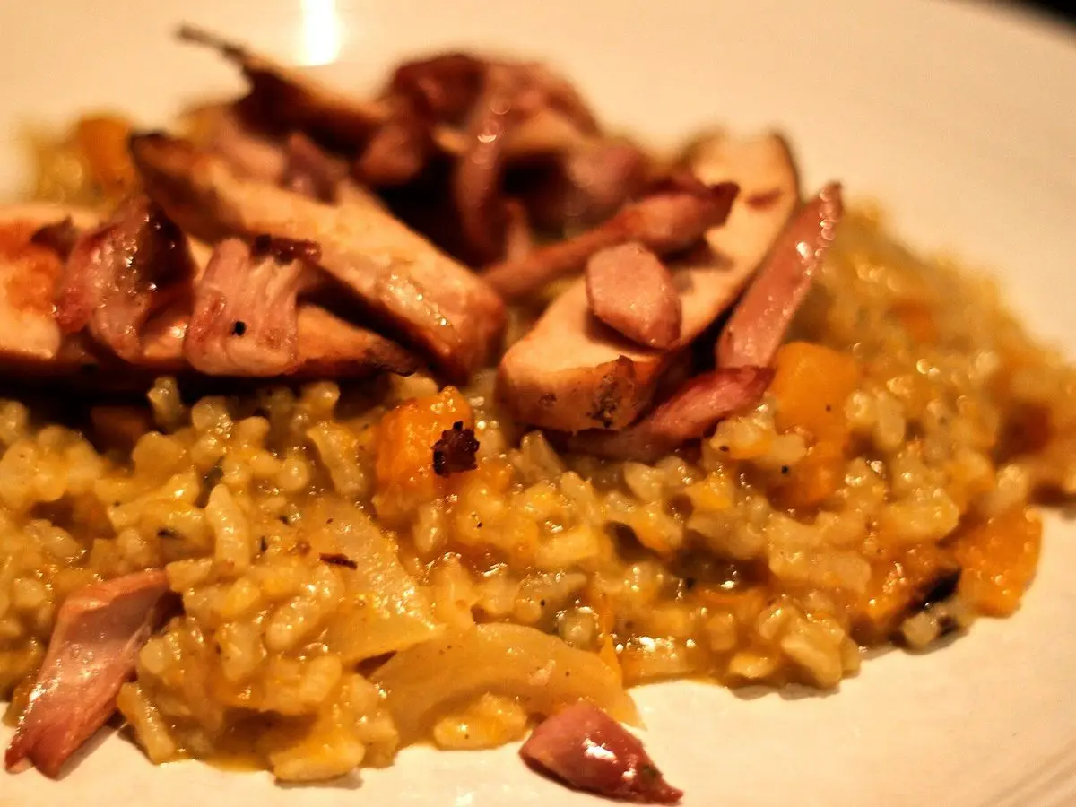 Risotto anaranjado con cebolla y lonchas de pollo ahumado por encima en primer plano