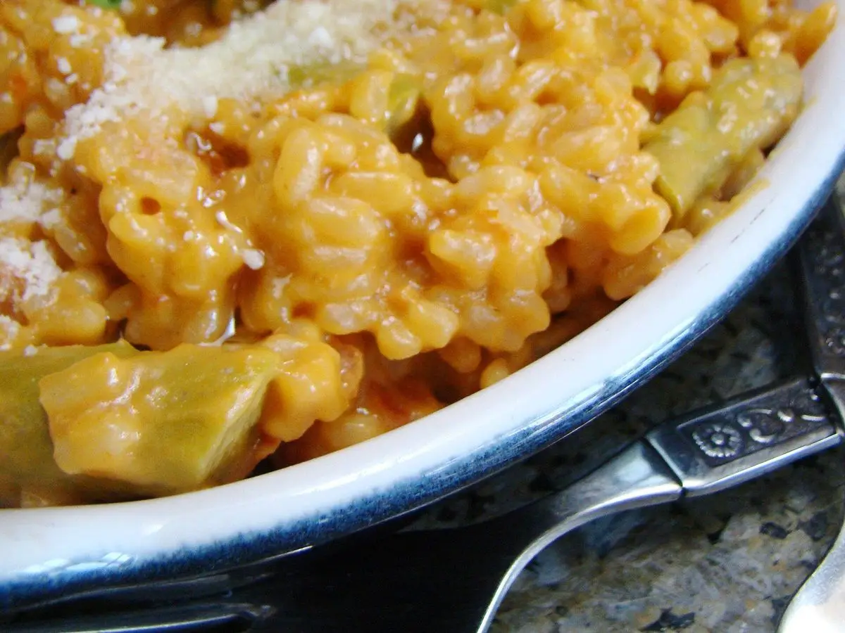 Plato de arroz cremoso con espárragos verdes y queso rallado por encima