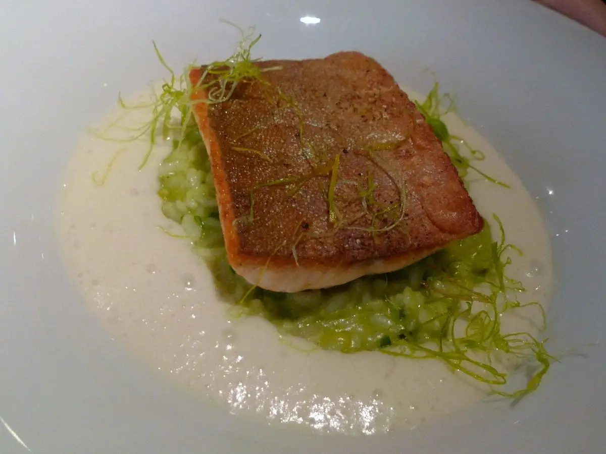 Filete de pescado con piel crujiente sobre risotto de puerro y verduras verdes en un plato hondo