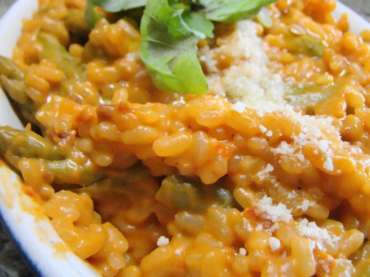 Risotto anaranjado de tomate con hoja de albahaca y queso rallado en un plato blanco