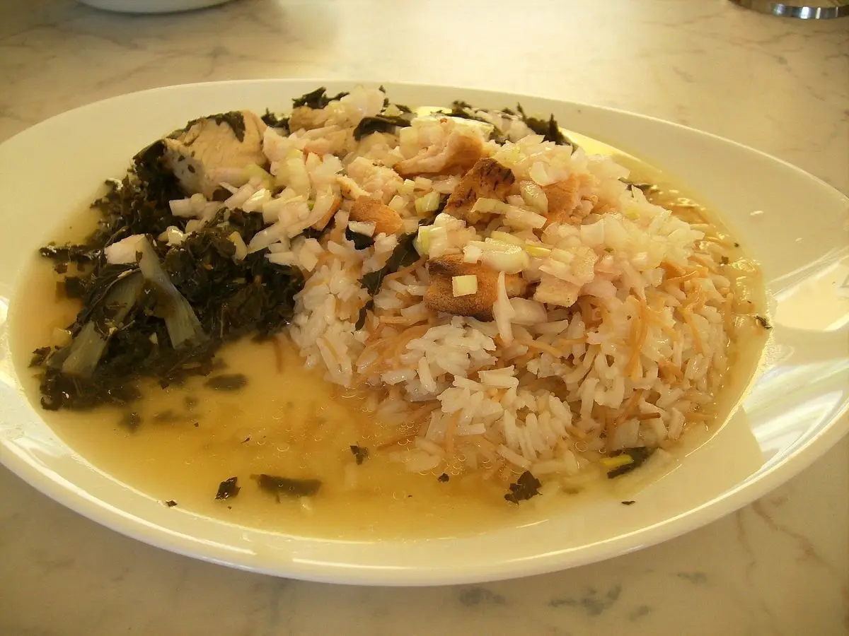 Plato ovalado de arroz blanco con pollo desmenuzado, zanahoria y hojas verdes en caldo