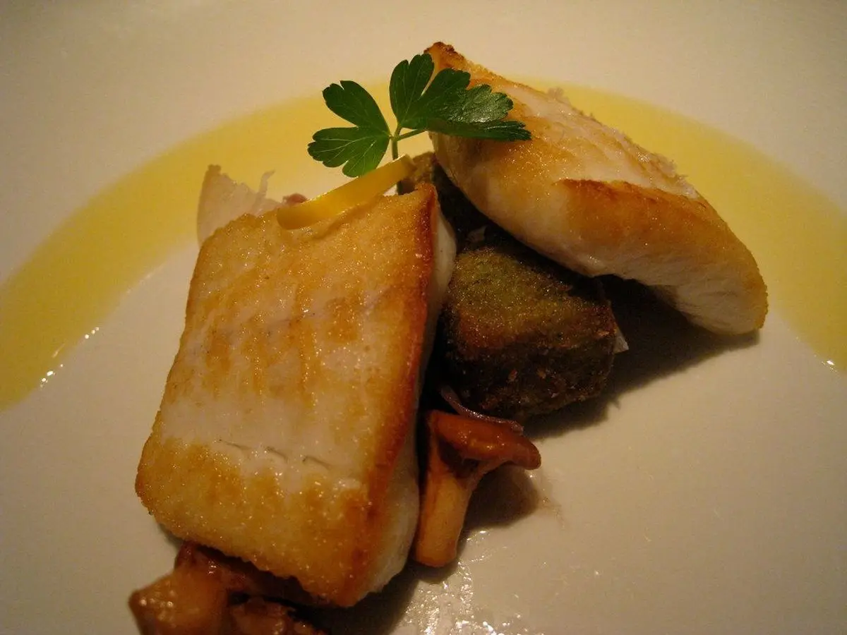 Filetes de pescado blanco dorado sobre salsa amarilla con patata salteada