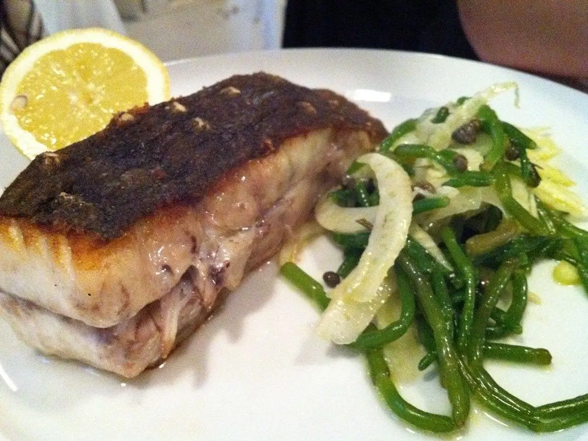 Lomo de rodaballo a la plancha con verduras verdes salteadas, cebolla y una rodaja de limón en un plato blanco