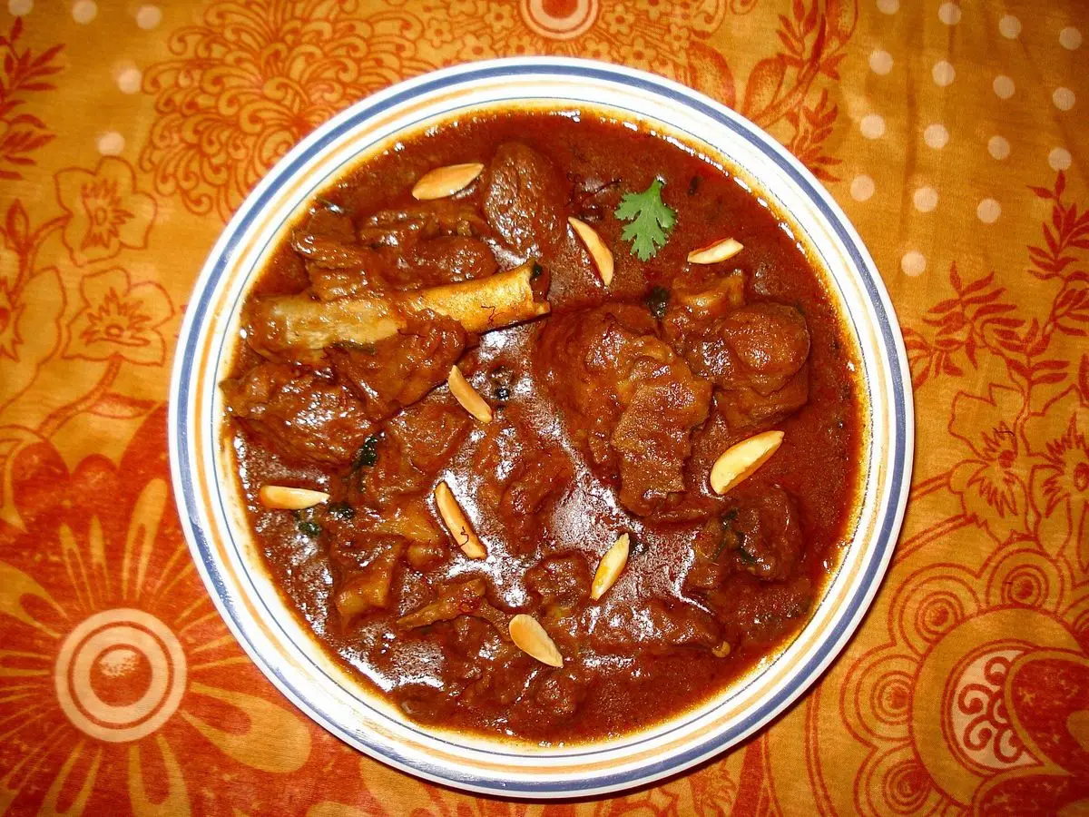 Cuenco de cordero guisado en salsa roja especiada con almendras laminadas sobre un mantel naranja