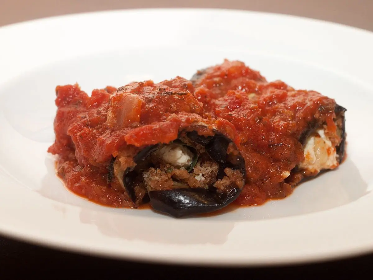 Rollito de berenjena relleno cubierto de salsa de tomate sobre un plato blanco