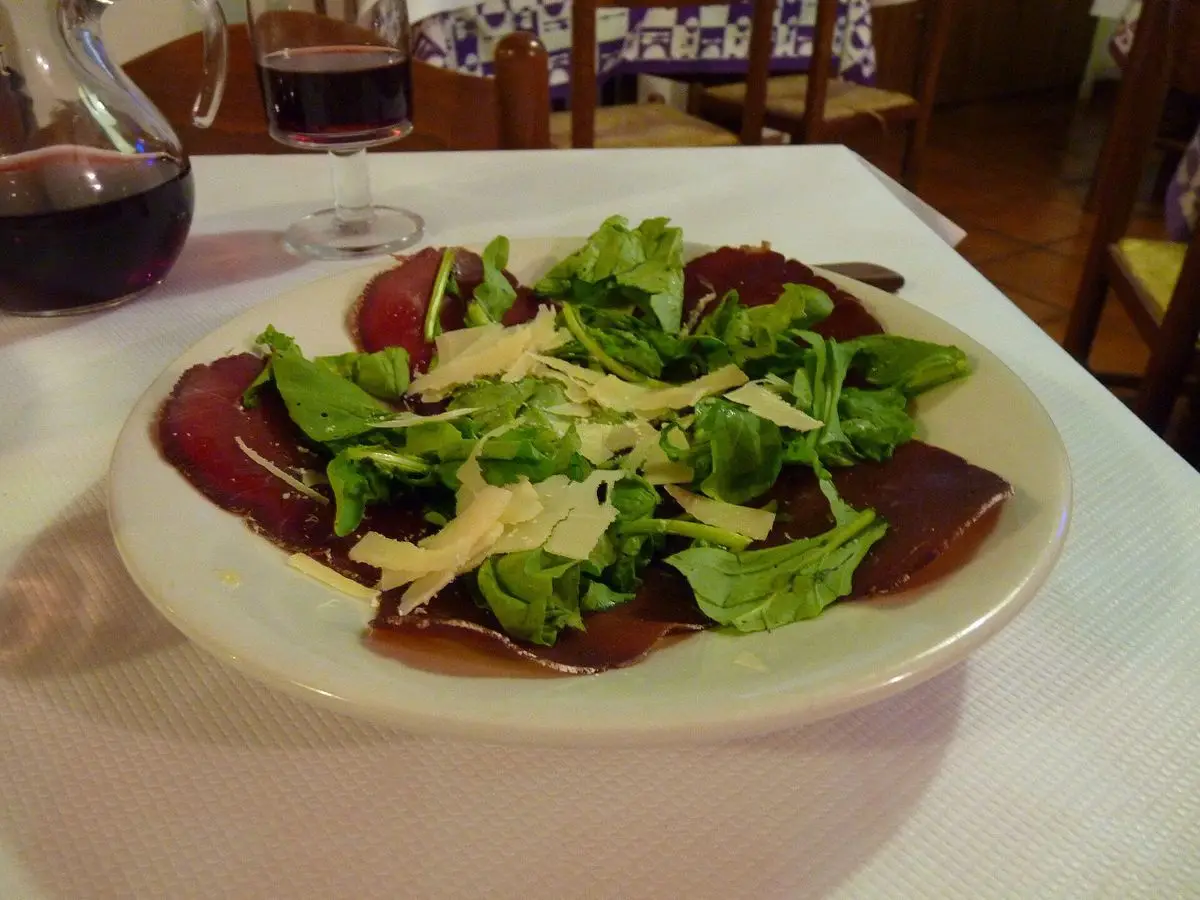 Plato de bresaola en lonchas finas con rúcula y virutas de parmesano sobre un mantel blanco