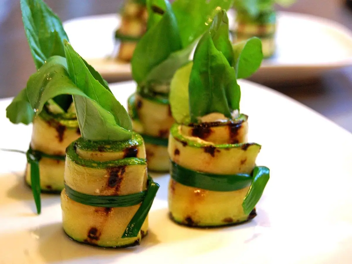 Rollitos de calabacín a la plancha atados con hierbas y rellenos, servidos sobre un plato blanco