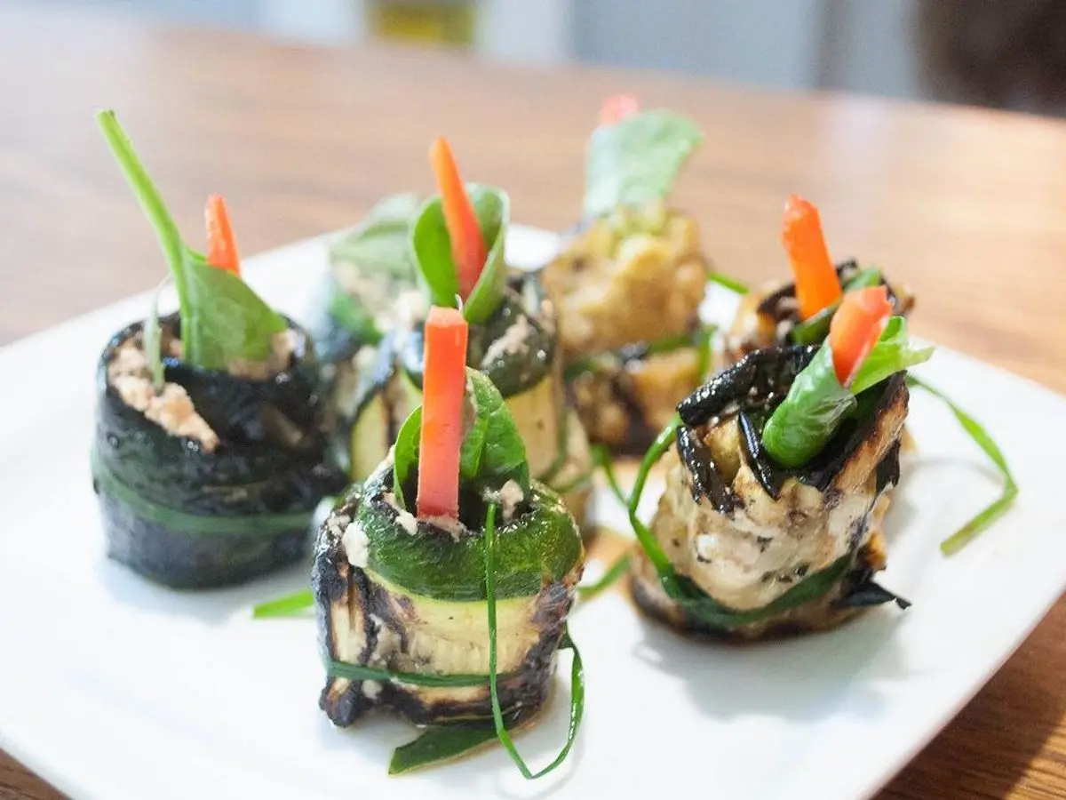 Rollitos de calabacín con tiras de zanahoria y verduras sobre un plato blanco